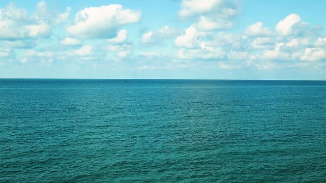Small fishing boat glides through calm blue waters near a rocky coastline, with distant mountains and a clear sky enhancing the peaceful coastal landscape