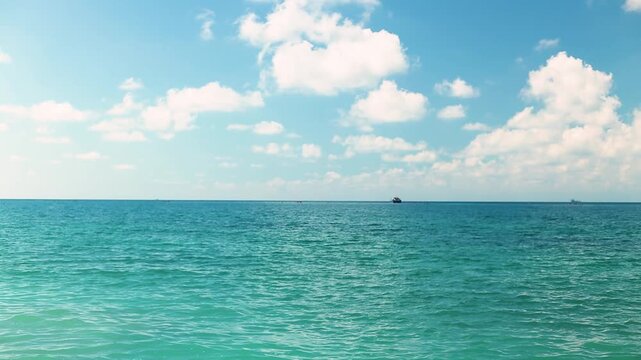 Small fishing boat glides through calm blue waters near a rocky coastline, with distant mountains and a clear sky enhancing the peaceful coastal landscape