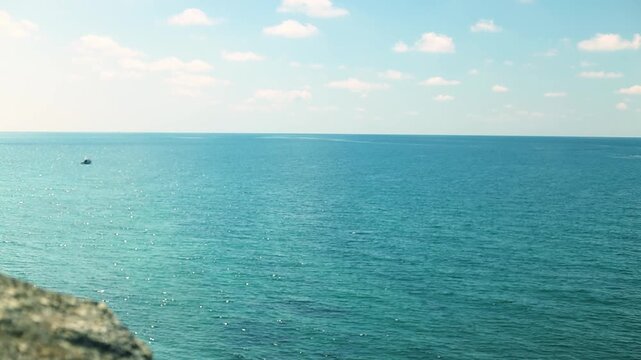 Small fishing boat glides through calm blue waters near a rocky coastline, with distant mountains and a clear sky enhancing the peaceful coastal landscape