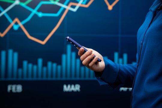 Businesswoman holding a smartphone in front of a glowing financial chart with bar graphs and rising trend lines.