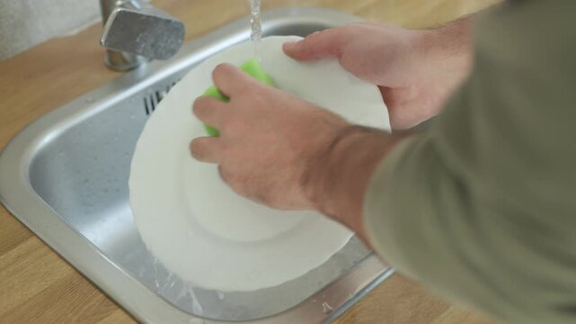 Washing ceramic plate with water and sponge in kitchen sink, male hands, domestic housework concept