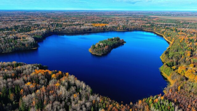 Aerial view of vibrant autumn forest surrounding tranquil blue lake and small island