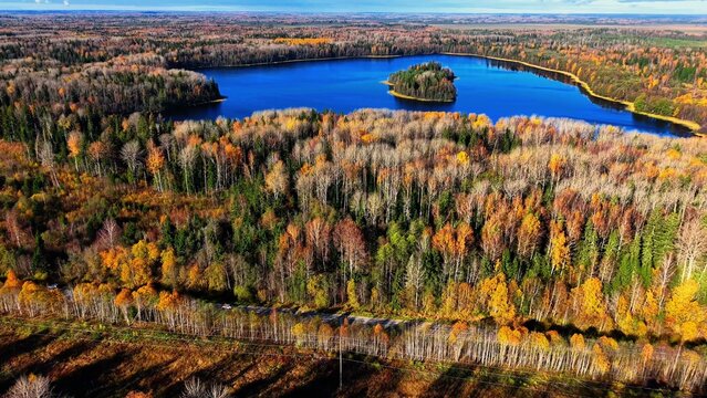 Aerial view of a vibrant autumn forest surrounding a serene blue lake and an island