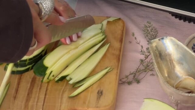Hands cutting zucchini into thin strips on a wooden board
