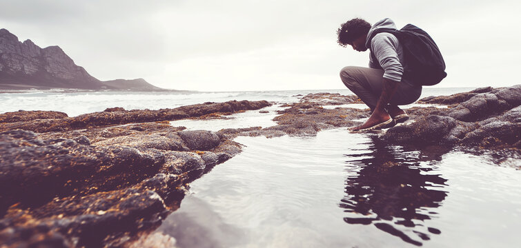 Man exploring tidal pool on a rugged coast, reflecting nature and discovering marine environment