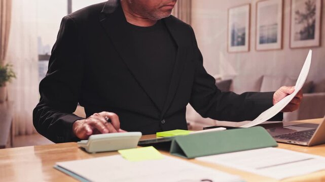 Mature businessman calculates financial statements, invoices receipts on desk at home office. Corporate tax planning, balance sheet audit review, household budget expense management strategy.