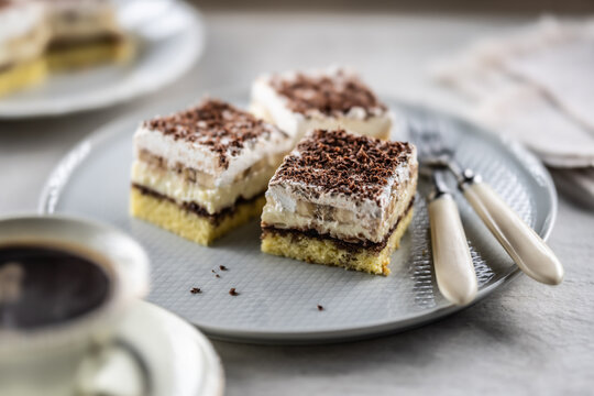 Delicious layered cakes with cream, bananas, and fluffy whipped cream served on an elegant plate. The top of the desserts is sprinkled with finely grated dark chocolate