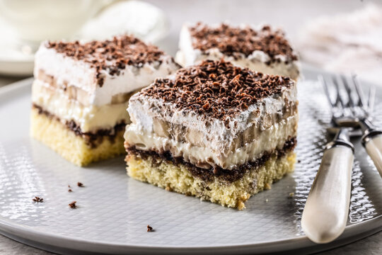 Delicious layered cakes with cream, bananas, and fluffy whipped cream served on an elegant plate. The top of the desserts is sprinkled with finely grated dark chocolate