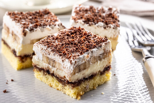 Delicious layered cakes with cream, bananas, and fluffy whipped cream served on an elegant plate. The top of the desserts is sprinkled with finely grated dark chocolate