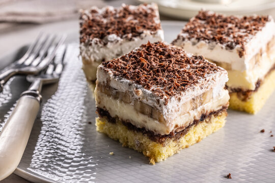 Delicious layered cakes with cream, bananas, and fluffy whipped cream served on an elegant plate. The top of the desserts is sprinkled with finely grated dark chocolate
