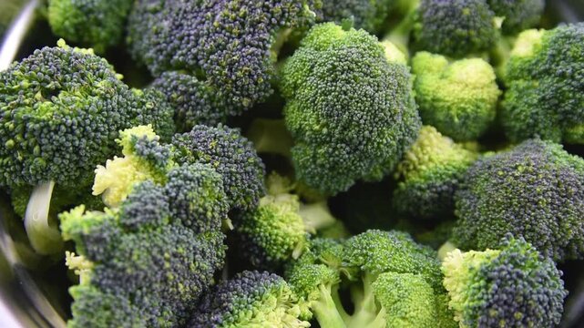 Close up view of raw fresh green broccoli florets in metal bowl and on wooden table surface background prepared for healthy vegan cooking.
