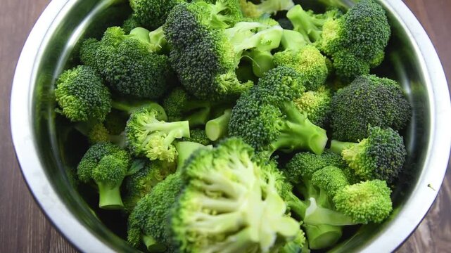 Close up view of raw fresh green broccoli florets in metal bowl and on wooden table surface background prepared for healthy vegan cooking.