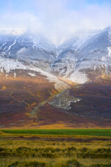 Scenic vertical landscape of majestic snow-capped mountain covered in clouds during autumn winter transition in Iceland. Majestic Nordic wilderness and nature background. © bank215