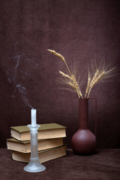 A brown vase with ears of wheat, a candle and a stack of books