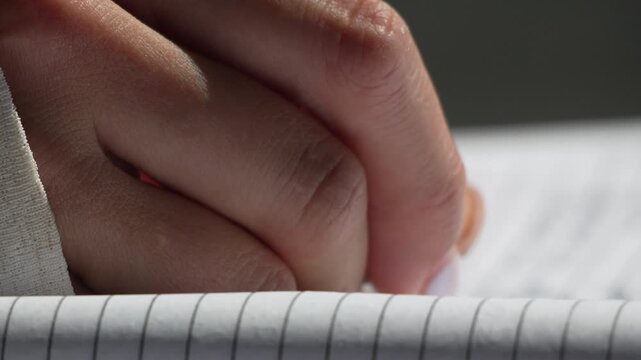 Handwriting close-up, a person writes notes with a black pen on a white lined notebook page. Extreme macro shot.