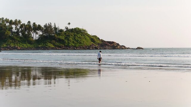 Man walking on Mandrem beach Goa India with palm trees and ocean