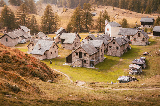 Dramatic wide view of the Crampiolo hamlet nestled among golden larches and rocky slopes