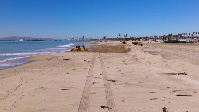 Long Beach, California, USA - October 15, 2026: Bulldozer spreads sand to raise the beach as excavator and dump trucks build a berm to shield the shore from flooding after Tropical Storm Rachel.