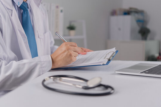 Doctor writing clinical notes with stethoscope and laptop