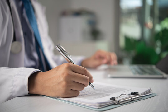 doctor hands writing on clipboard at desk with laptop