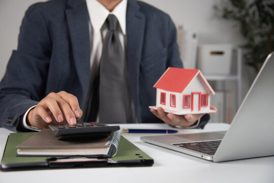Businessman holding a model house and uses a calculator and real estate finance in an office.