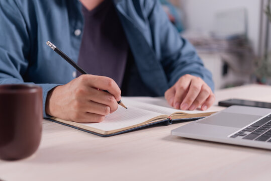 Person Writing Notes in Notebook Beside Laptop for Planning