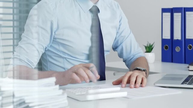 Mature businessman working on a laptop computer at his office desk, typing and focusing on business tasks with document binders and paperwork visible in the background