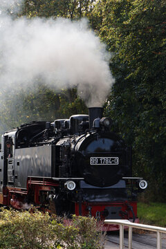 Historic vintage steam locomotive train riding on tracks emitting thick white smoke outdoors