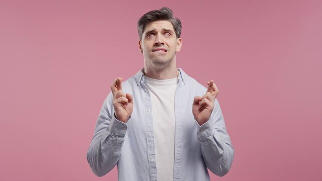 Handsome Man Crossing Fingers. Adult Guy Praying With Hopeful Expression, Silently Prays. Luck, important results, business risks On Pink