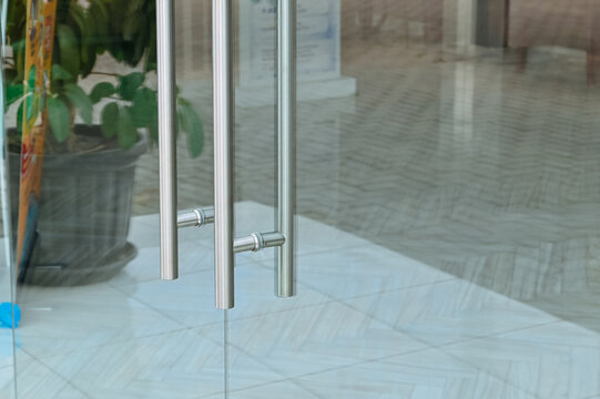 Close-up shot of modern stainless steel vertical door handles installed on a clear glass door of an office or commercial building.