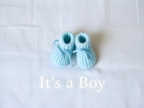 Its a Boy baby announcement banner with soft blue knitted booties on white linen