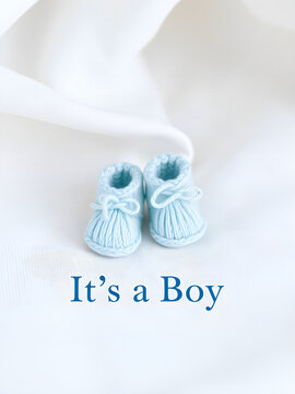 Its a Boy baby announcement banner with soft blue knitted booties on white linen