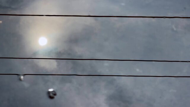 Reflection of sunlight and overhead electrical cables on gently rippling water, creating an abstract pattern of shimmering light and distorted lines