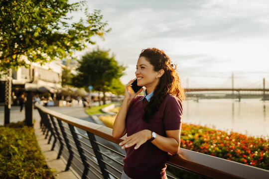 Woman smiling talking on smartphone along river promenade