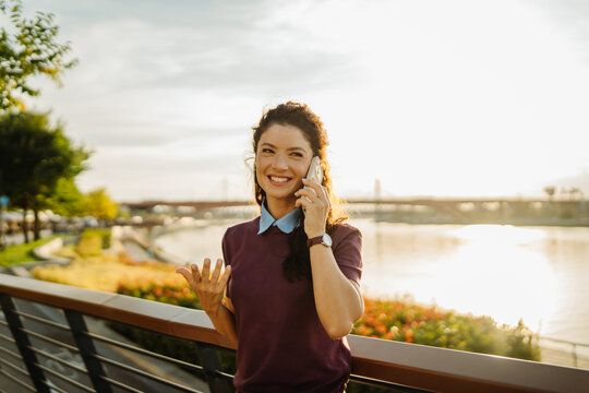 Woman talking on smartphone in city park at sunset