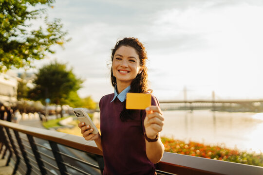 Woman showing credit card and phone outdoors
