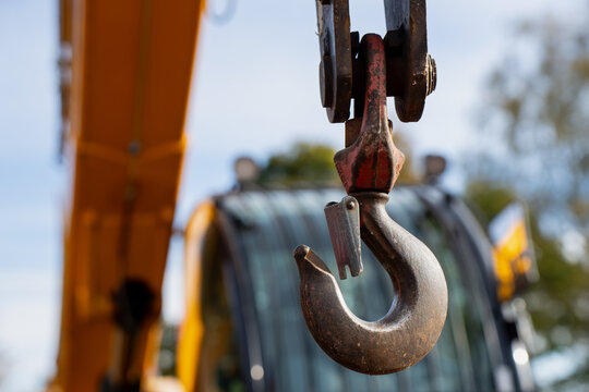 Suspended metal lifting hook with worn finish and a visible safety latch forms a load connection, illustrating rigging hardware for heavy equipment lifting applications
