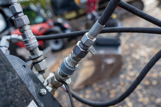 Metal hydraulic couplings connect flexible hoses to a mounted assembly, illustrating detachable fluid connections used in machinery servicing and attachment installation