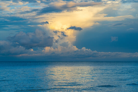 Clouds and water meet at sunset near the coast with light breaking through the clouds