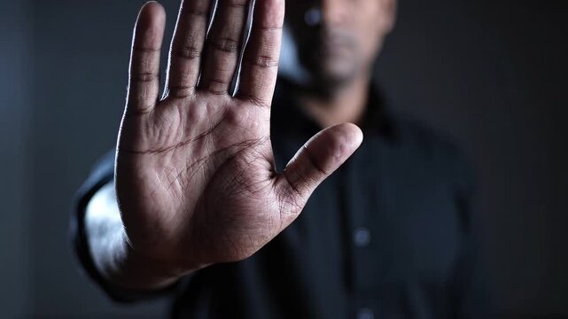 Man raising open palm in a stop gesture. Personal boundaries and refusal. Warning, rejection and consent concept. Close-up hand with person in background.