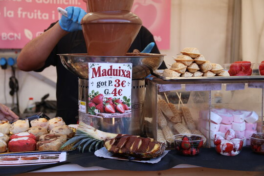 Puesto de postres y fuente de chocolate con fresas y frutas en un mercado gastron&oacute;mico al aire libre