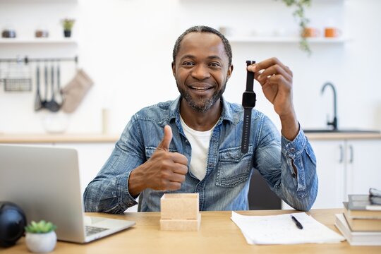 Smiling man presents a smartwatch at a table beside a laptop and notebook, suggesting a positive review of wearable technology at home