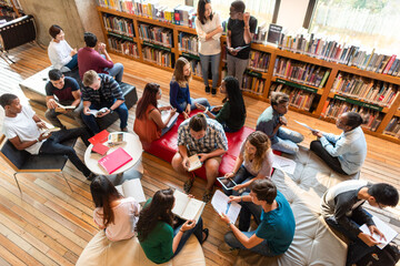 Naklejka na ściany i meble Diverse group of students studying in a library with books and tablets.