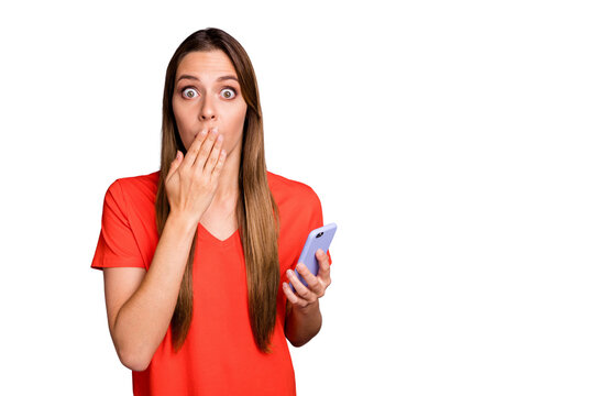 Portrait of negative shocked girl blogger social media user use cellphone share private information feel guilty close cover her mouth palm wear orange t-shirt isolated red color background