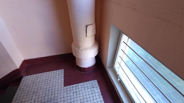 Garbage chute installed beside a barred window on a tiled apartment stairwell landing, illustrating residential waste disposal systems, sanitation and building maintenance