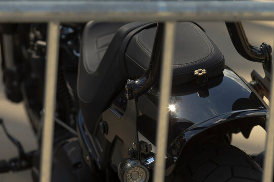 Close-up of rear section of black motorcycle showing passenger seat, chrome sissy bar, and rear fender through metal railing.