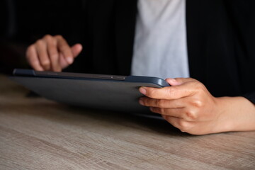 Close-up of a business professional in a black blazer holding a digital tablet horizontally at a wooden desk, representing mobile computing, online work and modern office technology. © Ojah