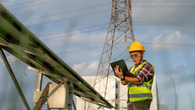 A qualified technician evaluates regional power distribution and renewable generation equipment outdoors under a clear sky.