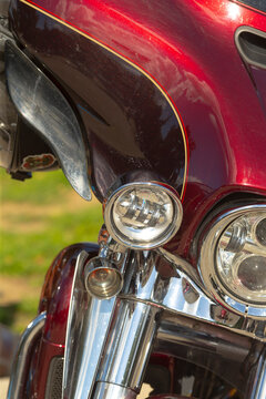 Close-up of front section of maroon motorcycle showing chrome headlights, fork, and painted fairing with pinstripe detail.