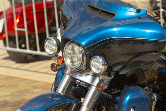 Close-up view of front fairing and triple headlights on blue touring motorcycle parked outdoors with metal fence in background.